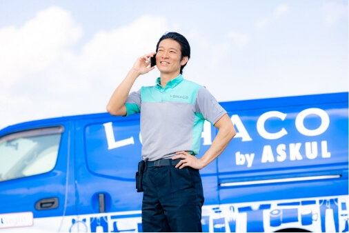 配送トラックの前に立ち、携帯電話で話をしているドライバー山本さんの写真